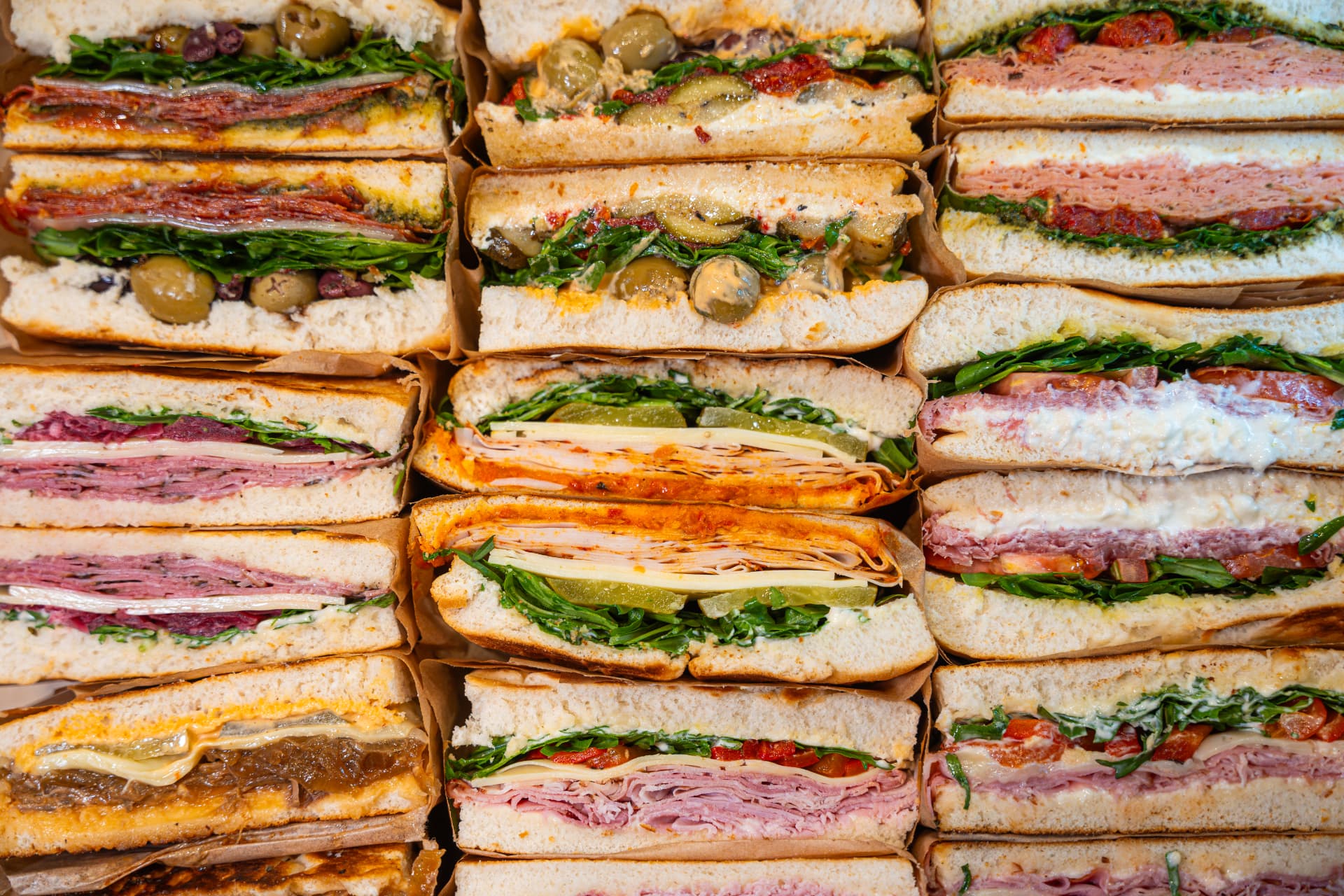 A wall of stacked Miro's Deli sandwiches showing fresh focaccia, cured meats and salads.